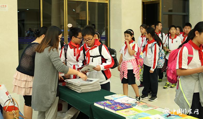 參加頒獎典禮的學生排隊入場，工作人員為他們分發(fā)當天的《文藝報》兒獎特刊